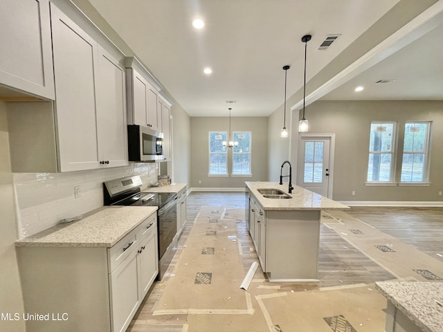 kitchen with pendant lighting, sink, a kitchen island with sink, stainless steel appliances, and light stone counters