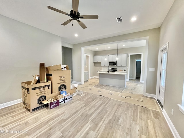 living room featuring ceiling fan, sink, and light wood-type flooring