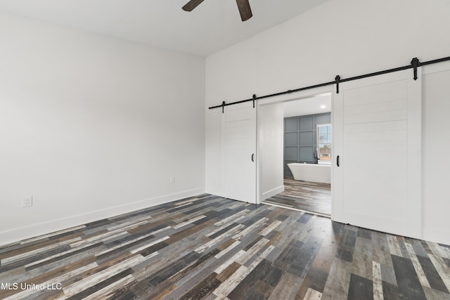 unfurnished bedroom featuring ensuite bathroom, a barn door, ceiling fan, dark hardwood / wood-style floors, and a closet