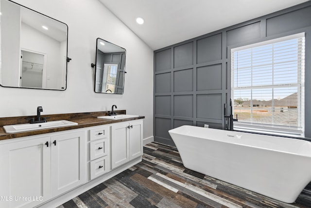 bathroom with hardwood / wood-style floors, a bath, lofted ceiling, and vanity