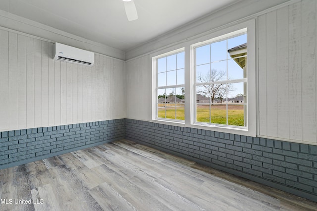 unfurnished room with ceiling fan, brick wall, a wall unit AC, and light wood-type flooring