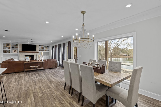 dining space featuring a fireplace, wood finished floors, baseboards, built in features, and crown molding