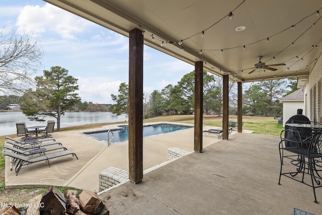 outdoor pool with a ceiling fan, a water view, and a patio