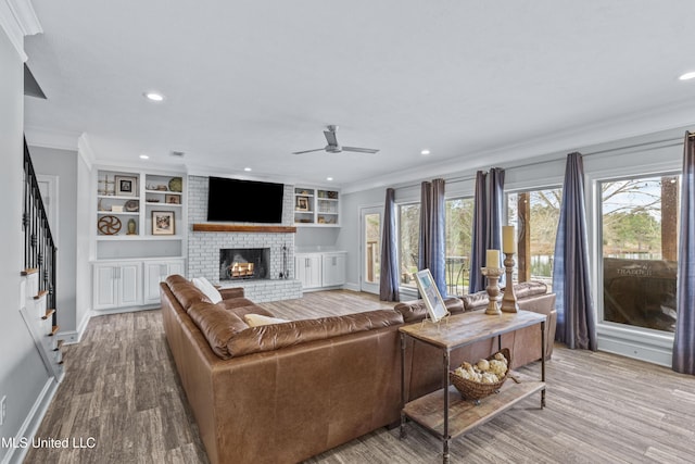 living room featuring crown molding, a brick fireplace, wood finished floors, baseboards, and stairs