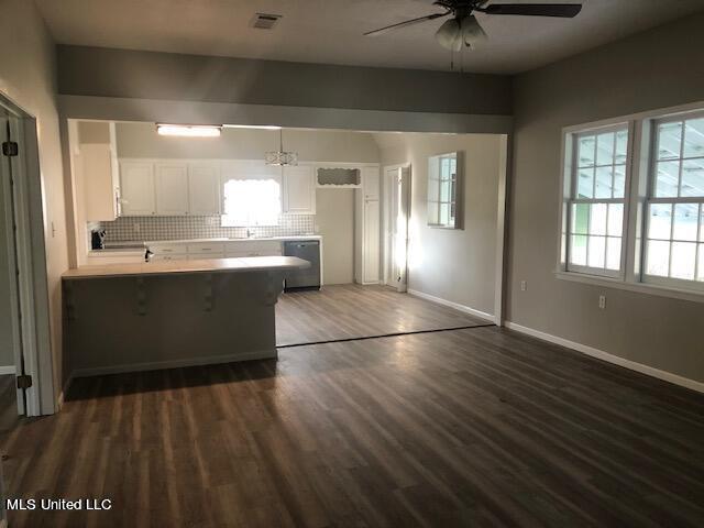 kitchen with dark wood-type flooring, tasteful backsplash, kitchen peninsula, a kitchen bar, and white cabinets