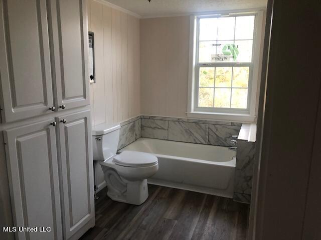 bathroom featuring crown molding, toilet, wood-type flooring, and a bath