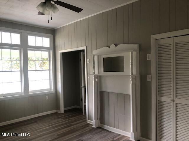 unfurnished bedroom featuring ceiling fan, a closet, wood walls, and dark hardwood / wood-style floors