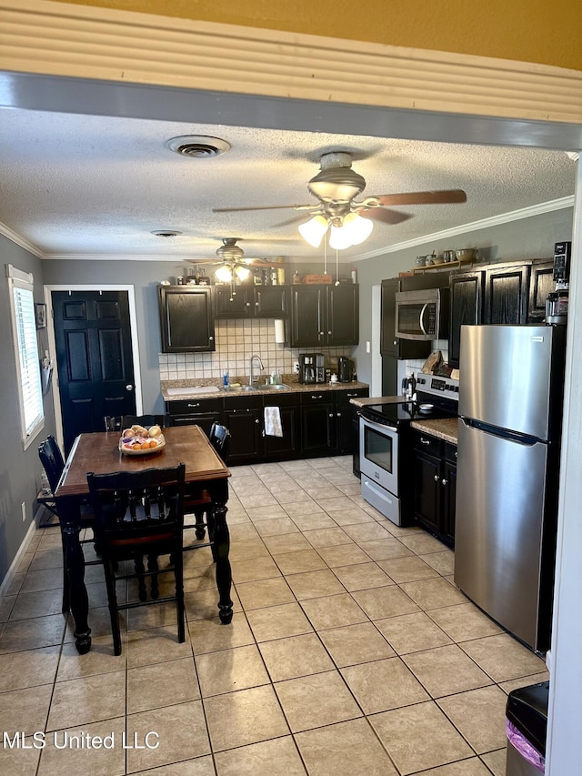 kitchen with light tile patterned floors, stainless steel appliances, dark cabinets, and crown molding