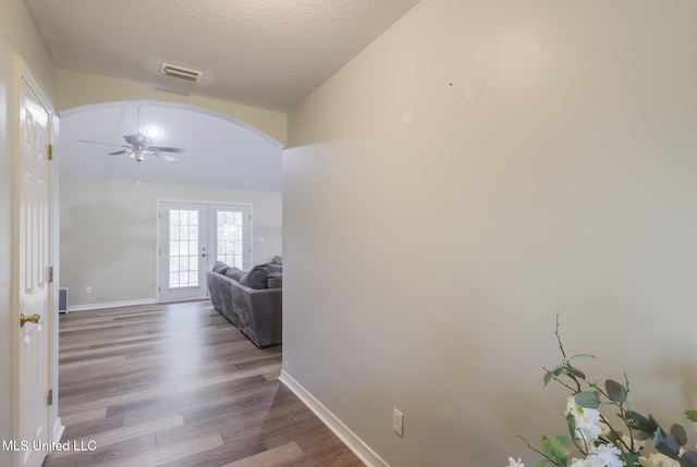 hallway with arched walkways, wood finished floors, french doors, baseboards, and a textured ceiling