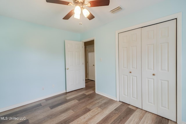 unfurnished bedroom with wood finished floors, a closet, baseboards, and a ceiling fan