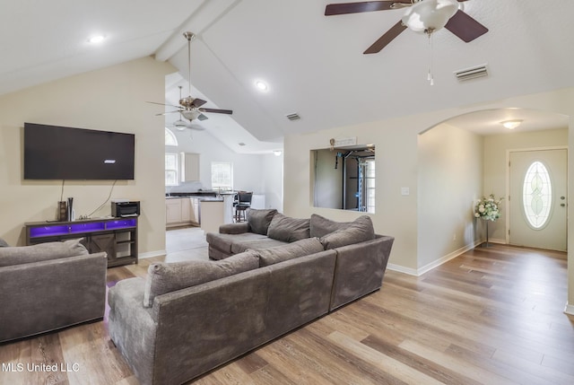 living room featuring a ceiling fan, arched walkways, plenty of natural light, beam ceiling, and light wood-type flooring