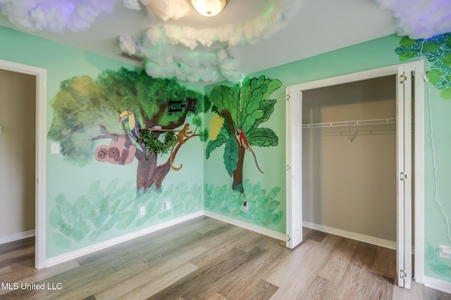 unfurnished bedroom featuring wood finished floors, baseboards, and a closet