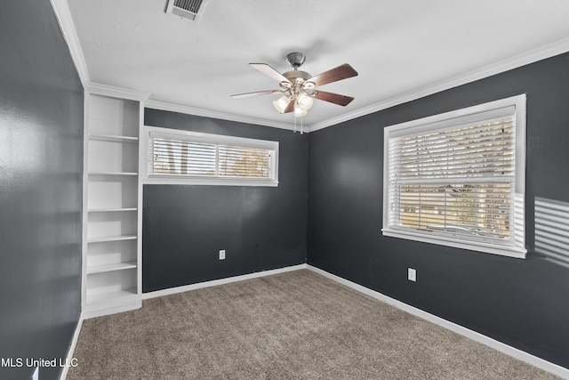 carpeted empty room with crown molding, a ceiling fan, visible vents, and baseboards