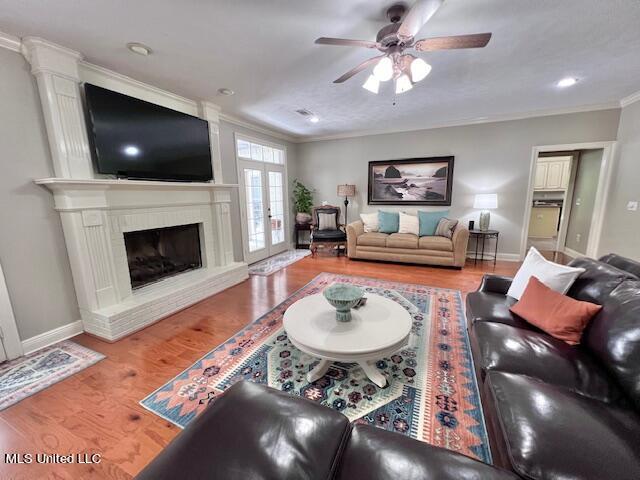 living room with french doors, a brick fireplace, ornamental molding, ceiling fan, and hardwood / wood-style floors