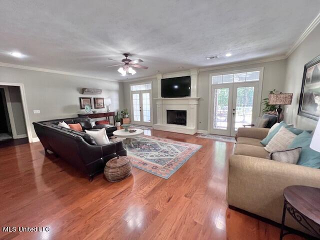 living room with crown molding, wood-type flooring, ceiling fan, and french doors