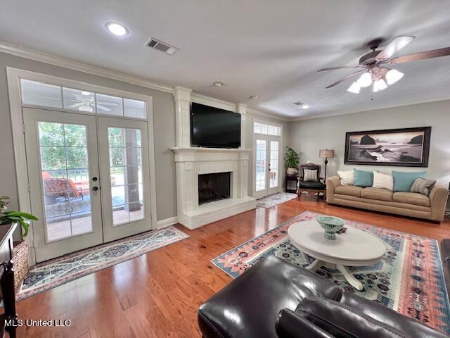 living room with crown molding, wood-type flooring, ceiling fan, and french doors