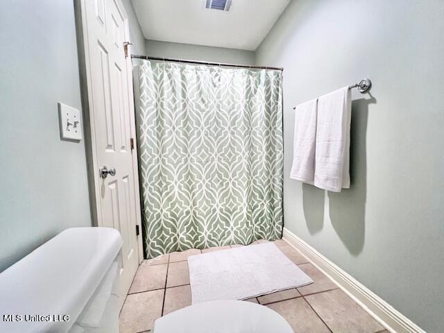 bathroom with toilet, curtained shower, and tile patterned flooring