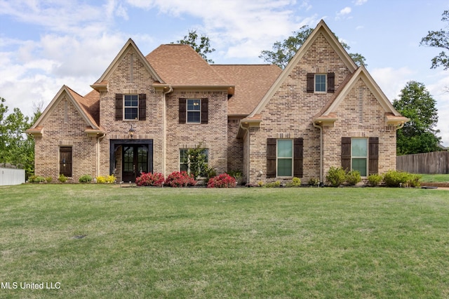 view of front facade with brick siding, a front lawn, and fence