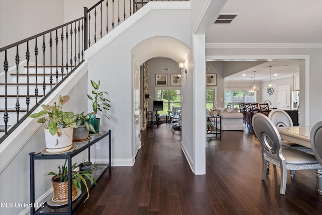 foyer with wood finished floors, crown molding, visible vents, baseboards, and arched walkways