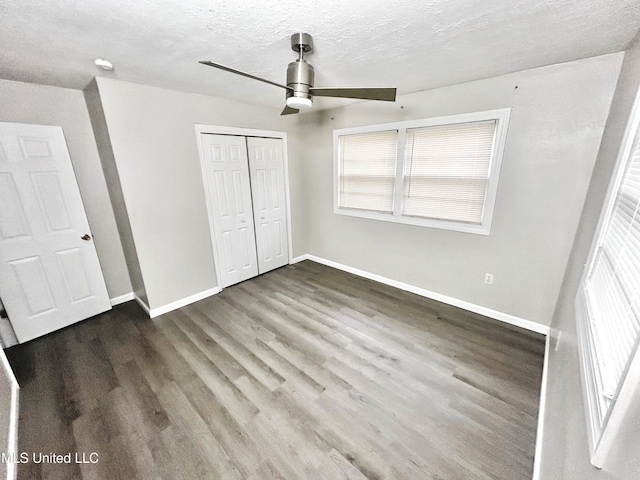 unfurnished bedroom featuring hardwood / wood-style floors, ceiling fan, a closet, a textured ceiling, and multiple windows