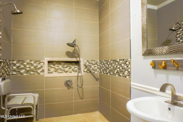 bathroom with a tile shower, ornamental molding, and a sink