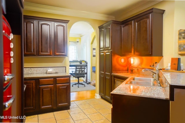 kitchen with arched walkways, light countertops, crown molding, and a sink