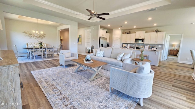 living room featuring ceiling fan with notable chandelier, light wood-type flooring, crown molding, and a tray ceiling