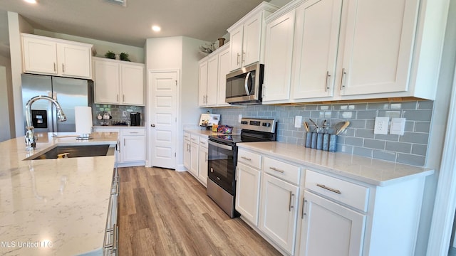 kitchen featuring sink, stainless steel appliances, light stone counters, light hardwood / wood-style flooring, and white cabinets