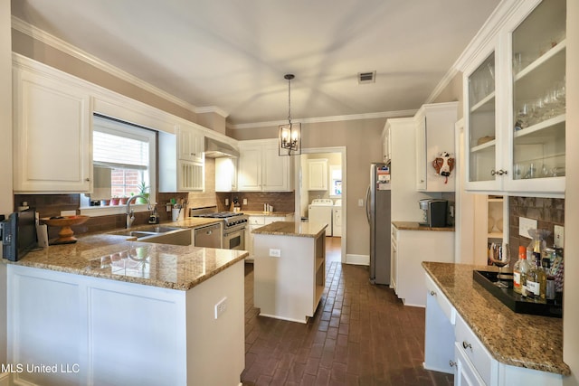 kitchen with backsplash, washer and clothes dryer, appliances with stainless steel finishes, brick floor, and a sink