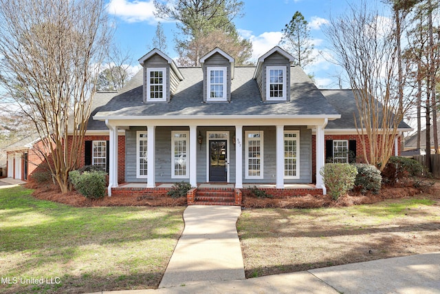 cape cod home featuring a shingled roof, a porch, brick siding, and a front lawn