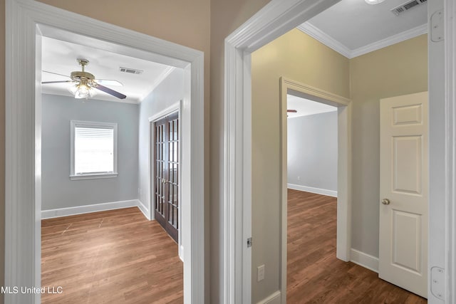 hall featuring visible vents, wood finished floors, baseboards, and ornamental molding