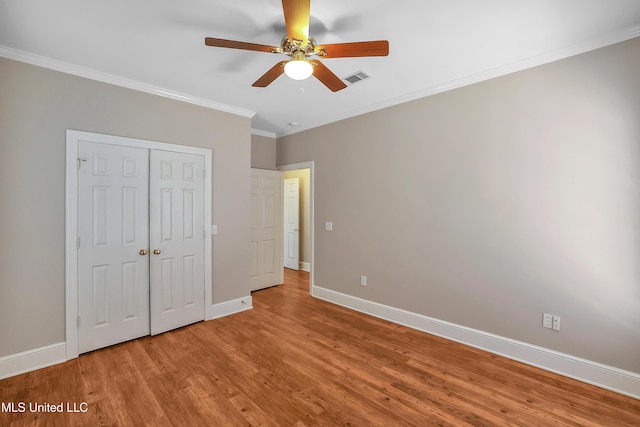 unfurnished bedroom with visible vents, ornamental molding, baseboards, and wood finished floors