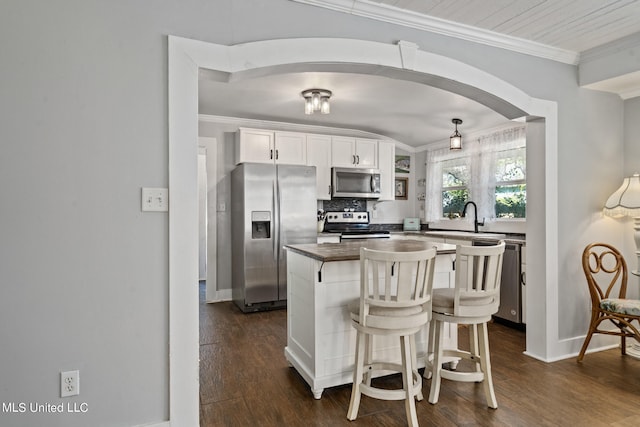 kitchen featuring crown molding, a breakfast bar, white cabinetry, appliances with stainless steel finishes, and dark hardwood / wood-style flooring