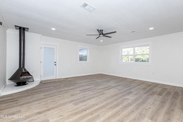 unfurnished living room with crown molding, light hardwood / wood-style flooring, a wood stove, and ceiling fan