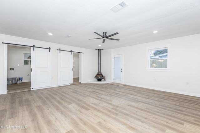 unfurnished living room with ceiling fan, crown molding, light wood-type flooring, and a barn door