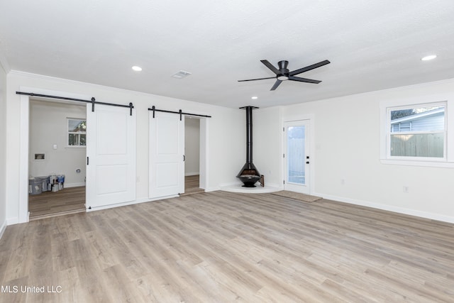 unfurnished living room featuring a barn door, a textured ceiling, ceiling fan, ornamental molding, and light hardwood / wood-style flooring