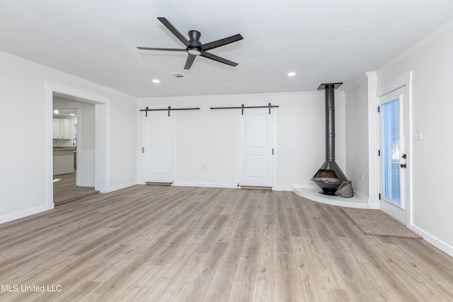 unfurnished living room featuring crown molding, light wood-type flooring, a barn door, and ceiling fan