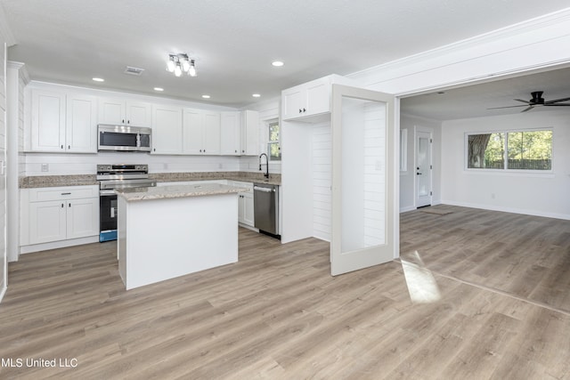 kitchen with a center island, white cabinets, light wood-type flooring, appliances with stainless steel finishes, and ceiling fan