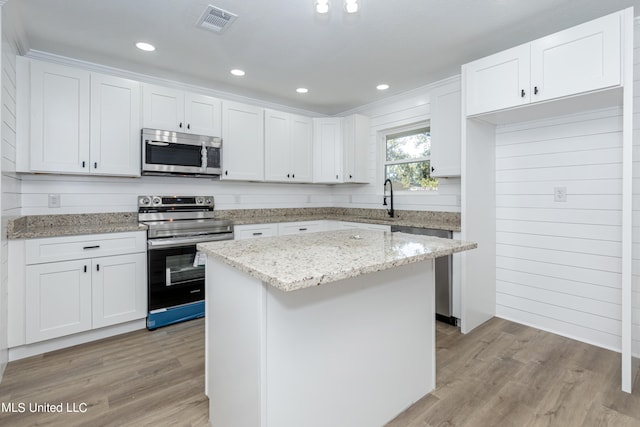 kitchen featuring appliances with stainless steel finishes, light hardwood / wood-style flooring, white cabinetry, and a center island