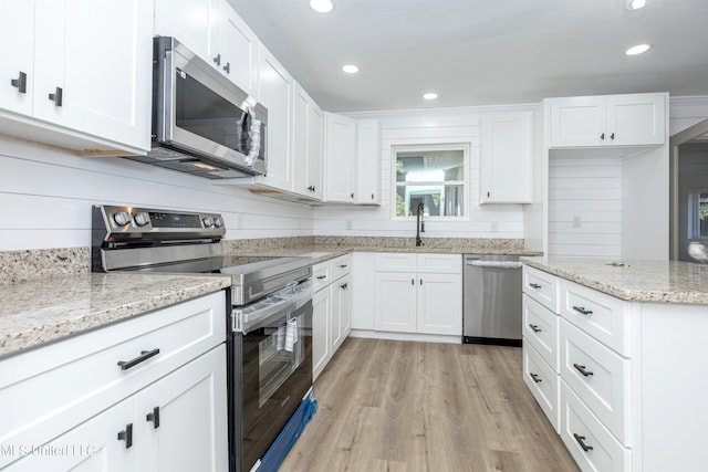 kitchen featuring light stone countertops, appliances with stainless steel finishes, sink, light wood-type flooring, and white cabinets