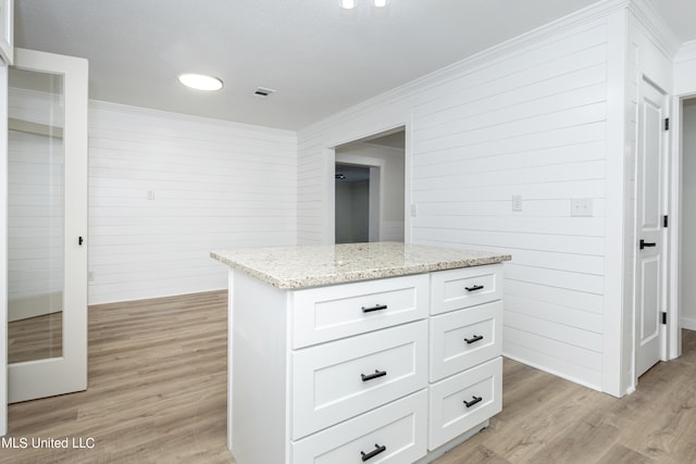 kitchen featuring ornamental molding, a center island, light stone countertops, white cabinets, and light hardwood / wood-style floors