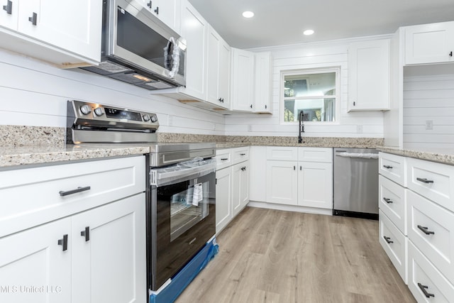 kitchen featuring light stone countertops, light hardwood / wood-style floors, appliances with stainless steel finishes, and white cabinets