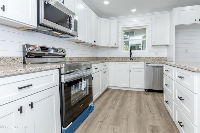 kitchen with light stone countertops, appliances with stainless steel finishes, light hardwood / wood-style flooring, and white cabinets