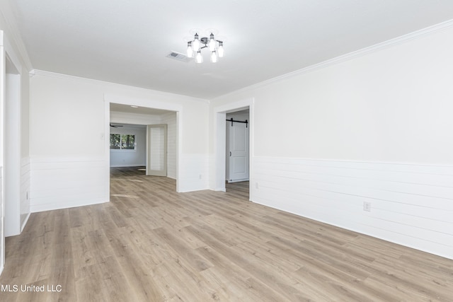 spare room with ornamental molding, light hardwood / wood-style flooring, and a barn door