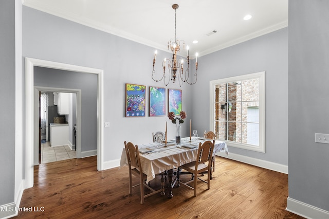 dining room with visible vents, wood finished floors, baseboards, an inviting chandelier, and ornamental molding