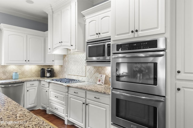 kitchen with white cabinets, stainless steel appliances, ornamental molding, and tasteful backsplash