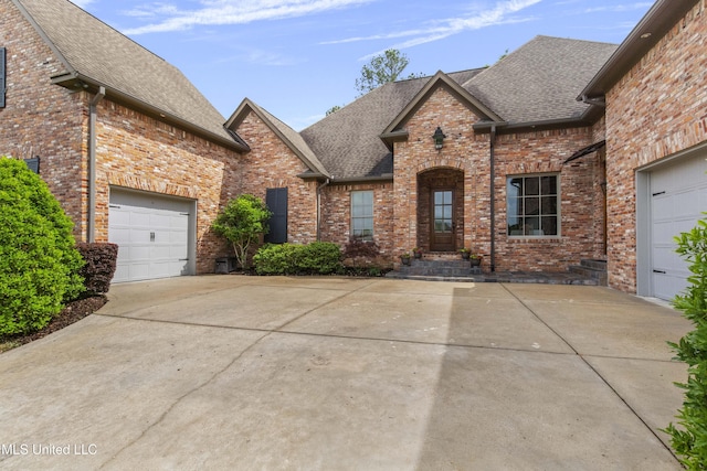 french country inspired facade with brick siding, roof with shingles, and concrete driveway