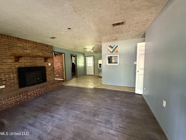 unfurnished living room with wood finished floors, a textured ceiling, a brick fireplace, and baseboards