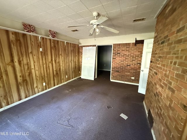 unfurnished room with ceiling fan, brick wall, baseboards, and wood walls