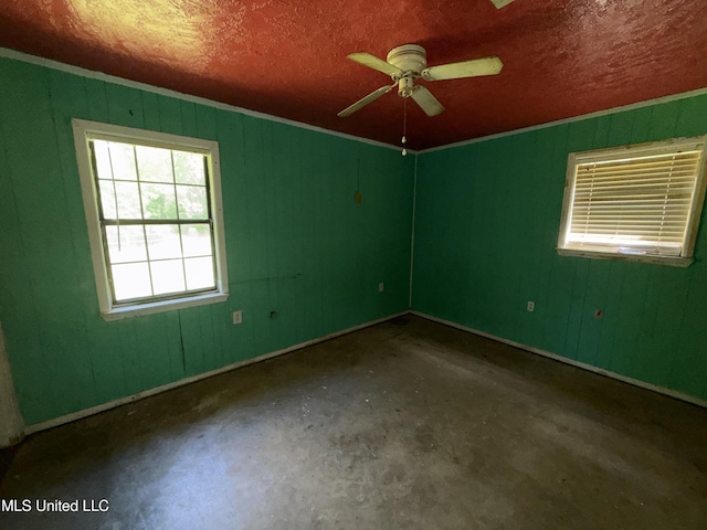 spare room featuring ceiling fan, unfinished concrete floors, baseboards, and wood walls